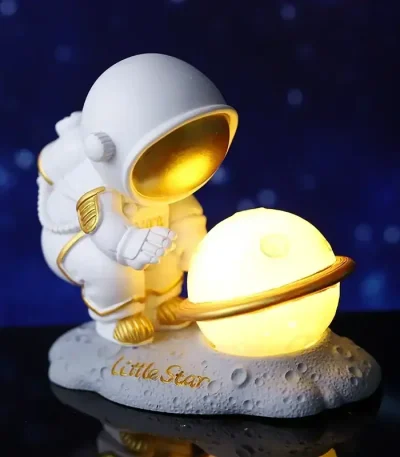 Figurina di astronauta in stile cartone animato che tiene un pianeta luminoso con anello, decorazione scientifica per ambienti interni.