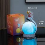 L'oggetto rappresenta un astronauta in piedi su una luna luminosa, con dimensioni di 15 cm di altezza e 8 cm di larghezza, ideale come decorazione scientifica o luce notturna.