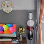 Orologio da parete con numeri grandi e sfondo bianco, decorazione di design con lampada a stelo moderna e fiori freschi in vasi, ambiente elegante e accogliente.