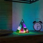 Lampada a piramide luminosa con effetti di luce colorata e sveglia vintage su scrivania in ambiente moderno.