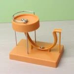 Pista di Rube Goldberg in plastica arancione con percorso curvo e palla metallica, ideale come oggetto decorativo o giocattolo scientifico educativo.