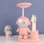 Pupazzo astronauta rosa con lampada da tavolo e decorazioni scientifiche, ideale come oggetto decorativo e da collezione per appassionati di scienza e spazio.