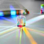 Cristallo ottico trasparente con riflessi di luce colorati, posizionato su una superficie bianca.