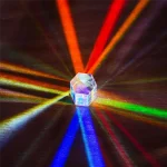 Palla di cristallo trasparente che riflette raggi di luce di vari colori, creando un effetto di dispersione luminosa su una superficie scura.