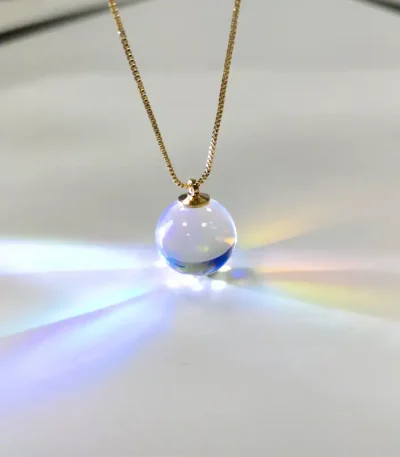 Pendente in vetro trasparente con effetto arcobaleno, sospeso su una delicata catena dorata, crea riflessi di luce colorati. Perfetto come gioiello decorativo e oggetto scientifico artistico.