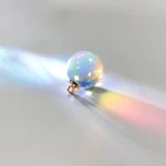 Pendente con sfera di cristallo iridescente che riflette luci colorate, appoggiato su una superficie chiara.
