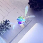 Cristallo decorativo di oggetto scientifico con riflessi iridescenti, posizionato su carta bianca con foglie e pigne intorno, ideale come decorazione da collezione o da scrivania.