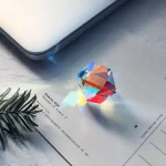 Prisma di vetro che proietta un arcobaleno di luce su carta e laptop, creando un effetto di rifrazione e riflesso colorato.