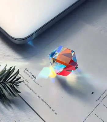 Prisma di vetro che proietta un arcobaleno di luce su carta e laptop, creando un effetto di rifrazione e riflesso colorato.