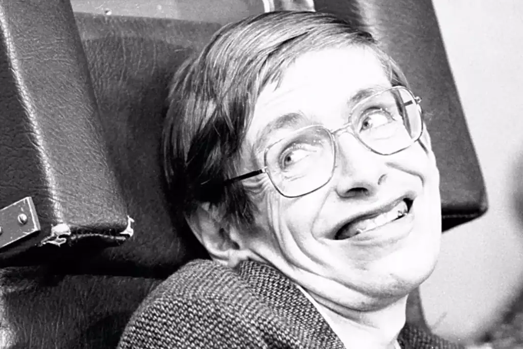 Ritratto in bianco e nero di un uomo sorridente con occhiali, seduto su una sedia, in un ambiente professionale o accademico.