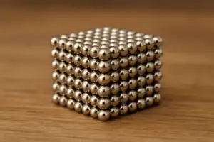 Cubo di sfere di magneti metallici argentati impilati, oggetto decorativo scientifico su superficie di legno.