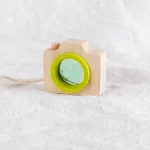 Fotocamera giocattolo in legno con lente verde, perfetta come decorazione scientifica o oggetto educativo per bambini. Design semplice e naturale, ideale per ambienti didattici o decorativi.