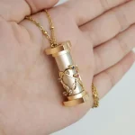 Collana con pendente a forma di tubo con decorazione a forma di DNA in oro e pietre colorate, simbolo di scienza e biologia.