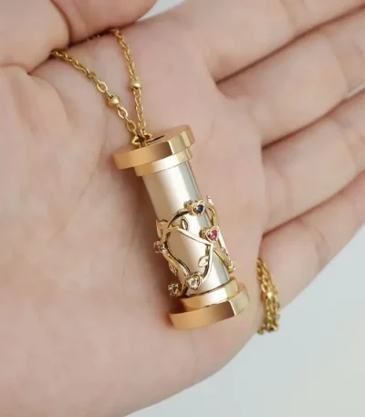 Collana con pendente a forma di tubo con decorazione a forma di DNA in oro e pietre colorate, simbolo di scienza e biologia.