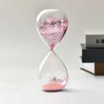 Orologio a sabbia decorativo con sabbia rosa e dettagli argentati, perfetto come oggetto scientifico e decorativo per ambienti moderni e studi.