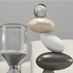 Oggetto decorativo in pietra e vetro, equilibrato in una composizione artistica su una superficie bianca.