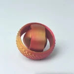 Anello in metallo con superficie testurizzata e rivestimento colorato, utilizzato come oggetto decorativo scientifico o come modello didattico.