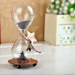 Orologio a clessidra decorativa con sabbia nera, base in legno e dettagli in metallo, perfetto come oggetto di arredamento scientifico e decorativo.