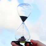 Orologio a clessidra con sabbia nera e trasparente, simbolo di tempo e scienza, ideale come decorazione scientifica.
