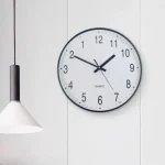 Orologio da parete con quadrante bianco e numeri neri, design semplice e moderno, ideale per ambienti di studio o ufficio.