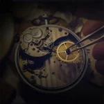 Dettaglio di un orologio meccanico con ingranaggi e ruote visibili, mentre un artigiano utilizza strumenti di precisione per la riparazione.