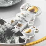 Modello di astronauta in miniatura con dettagli dorati, rappresentato su una superficie bianca, simbolo di esplorazione spaziale e curiosità scientifiche.