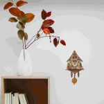 Vaso bianco con rami di foglie autunnali e orologio a cucù decorativo appeso alla parete, perfetto come oggetto decorativo scientifico.