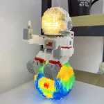 Scultura LEGO di un astronauta nello spazio con pianeta e stelle illuminate, decorazione scientifica originale e colorata.