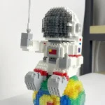 Modello di astronauta Lego in bianco con casco nero, seduto su una base arcobaleno colorata, decorazione scientifica e oggetto da collezione.
