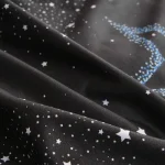 Tessuto nero con stampa di stelle bianche e blu, perfetto per decorazioni e abbigliamento scientifico.