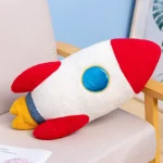 Peluche a forma di razzo spaziale con dettagli rossi, gialli e blu, ideale come decorazione scientifica o giocattolo educativo.