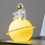 Decorazione spaziale con astronauta in piedi su una sfera luminosa gialla, perfetta come oggetto decorativo scientifico o da scrivania.