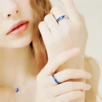 Anello scientifico blu con dettagli in argento, indossato su un dito di una donna con mani delicate e unghie curate, perfetto come decorazione o oggetto di collezione.