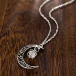 Collana con pendente a forma di luna e stella in argento, decorata con dettagli intricati, appesa a una catena sottile, su superficie di legno scuro.