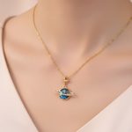 Collana con pendente pianeta e stella in oro, decorata con pietre blu e dettagli dorati, perfetta come gioiello ispirato allo spazio e alla scienza.