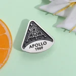 Spilla commemorativa Apollo 1969 con design di un razzo spaziale e la scritta "APOLLO 1969" su sfondo bianco e nero.