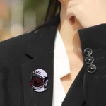 Pulsante decorativo con design astronauta e teschio, ideale per personalizzare abbigliamento e accessori con stile scientifico e innovativo.