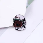 Spilla decorativa con casco spaziale, cane e simboli sovietici, perfetta come oggetto scientifico o decorativo. Ideale per appassionati di scienza, spazio e storia sovietica.