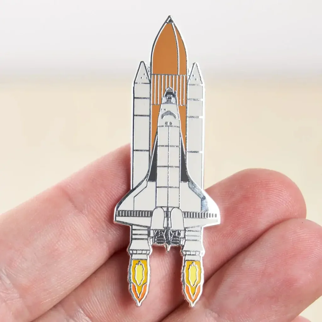Spilla a forma di razzo spaziale in metallo con dettagli colorati, perfetta come decorazione scientifica o accessorio per appassionati di spazio e tecnologia.