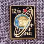 Piastrina in metallo con design spaziale, raffigura un astronauta e un pianeta con anelli, simbolo delle missioni spaziali italiane del 1961.