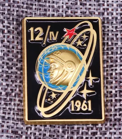 Piastrina in metallo con design spaziale, raffigura un astronauta e un pianeta con anelli, simbolo delle missioni spaziali italiane del 1961.