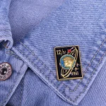 Pendente decorativo a tema spaziale applicato sulla tasca di una giacca jeans, con dettagli di un pianeta e un razzo, simbolo di esplorazione e avventura scientifica.