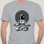 T-shirt grigia con stampa di un astronauta in stile cartone animato seduto, con sfondo di un fiore della vita, perfetta per appassionati di scienza e spazio.