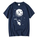 Maglietta blu con stampa di astronauta che tiene una luna come altalena, sfondo stellato, stile artistico divertente e originale.