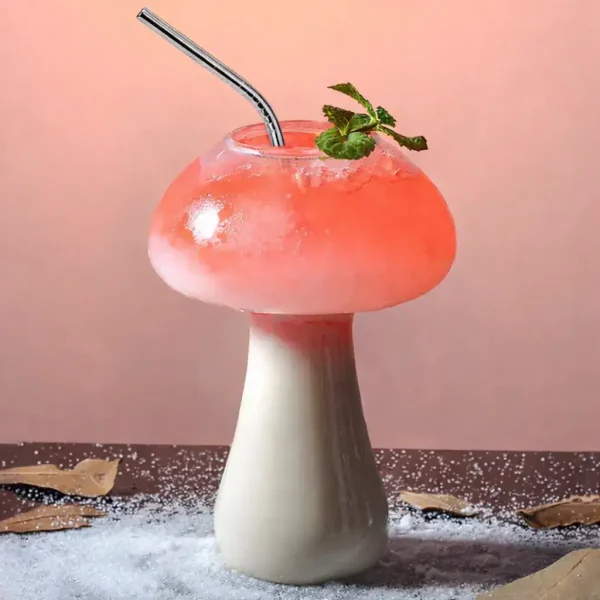 Bicchiere a forma di fungo con cocktail rosa, decorato con foglie di menta e cannuccia, su sfondo rosa pastello.