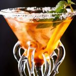 Cocktail decorato con elementi scientifici, come provette e strumenti da laboratorio, in un bicchiere elegante con sale sul bordo e foglie di menta, perfetto per eventi tematici.