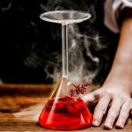 Pipetta di laboratorio con liquido rosso fumante, utilizzata per esperimenti scientifici, su superficie di legno.