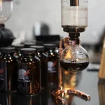 Immagine di un esperimento chimico con apparecchiature di laboratorio, tra cui un distillatore e bottiglie di reagenti, in un ambiente scientifico.