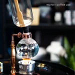 Sifone scientifico per preparare il caffè, con vetro e componenti in rame, in un ambiente da laboratorio o cucina moderna.