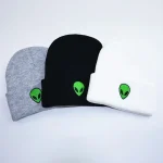 Cappelli in tessuto grigio, nero e bianco con stampa di alieno luminoso verde, ideali come accessori decorativi e per eventi a tema spaziale.
